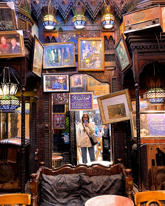 A room with a collection of old furniture and pictures. A mirror in the background reflects the photographer..